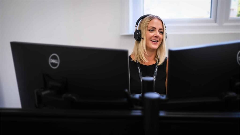 Gemma smiling between two monitors at her desk