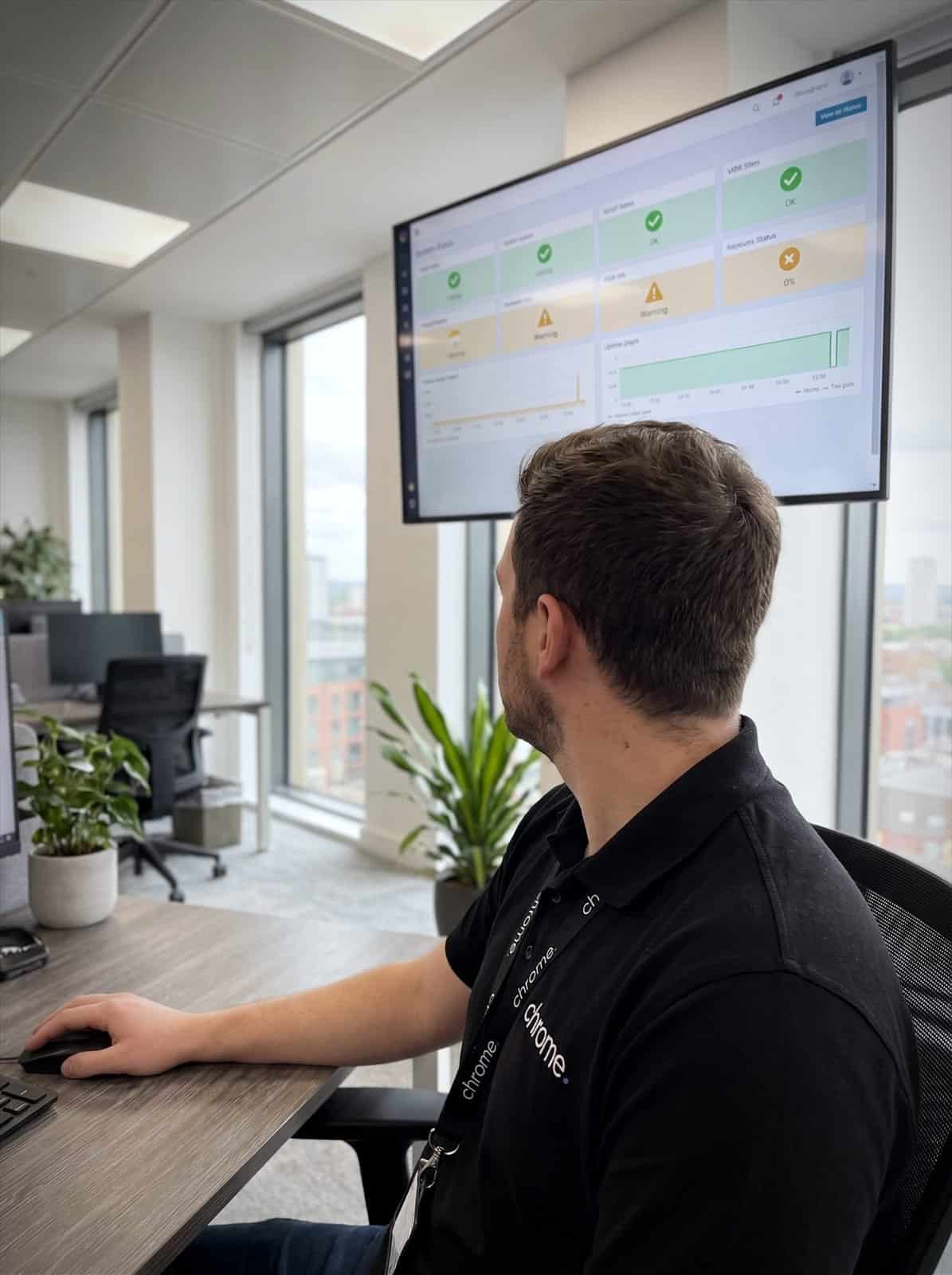 A Chrome Telecom engineer watches a live system status wallboard showing uptime and service indicators
