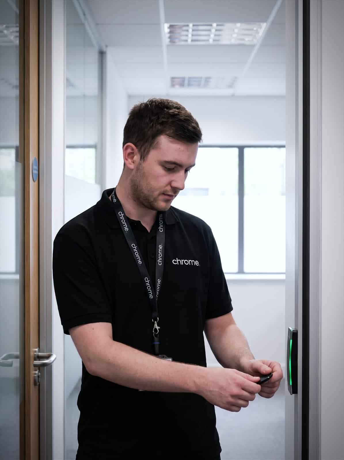 A Chrome Telecom engineer tests a door access reader with a key fob, the indicator showing green