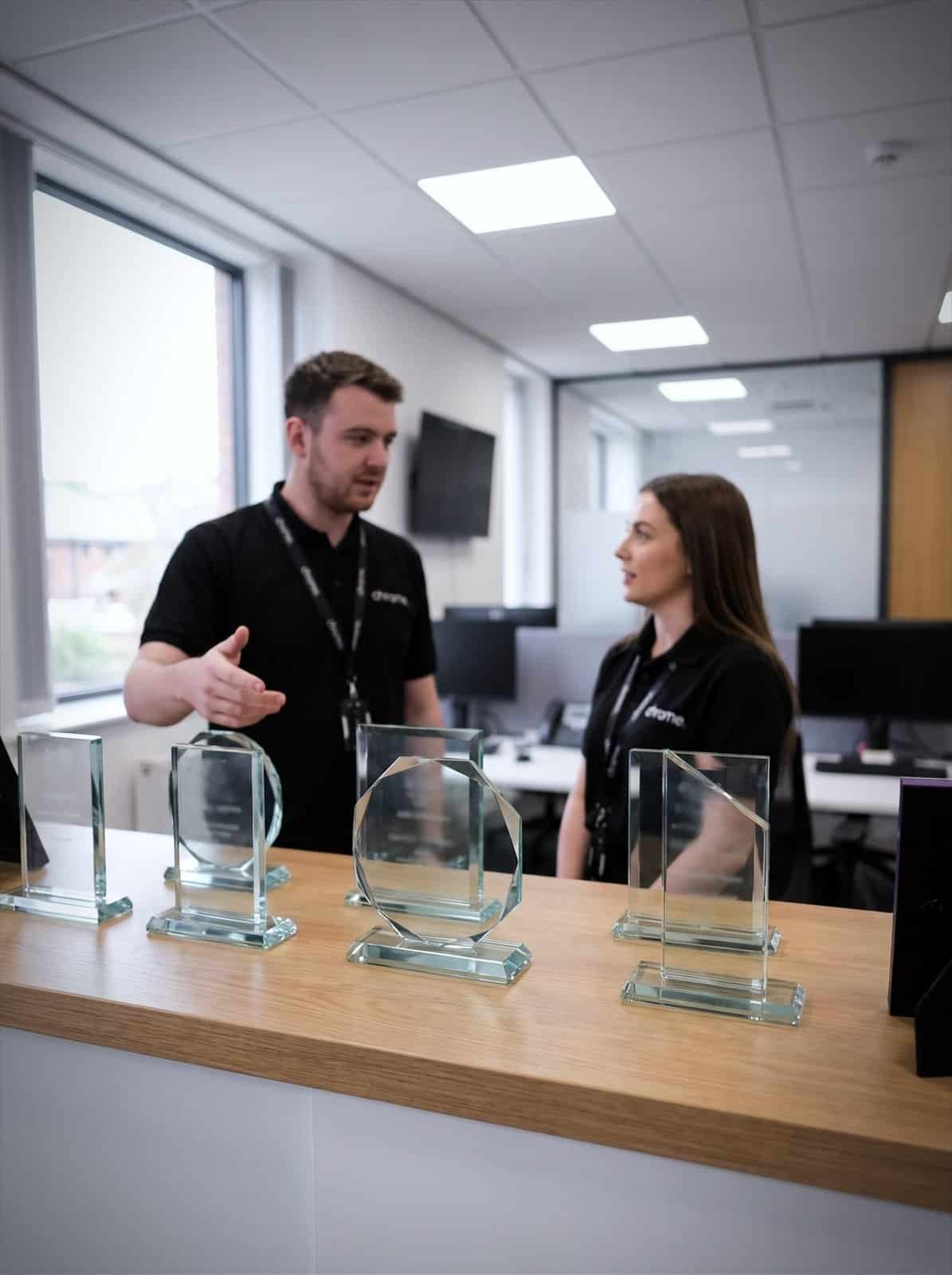 Award trophies on a shelf in the Chrome Telecom office with colleagues talking behind