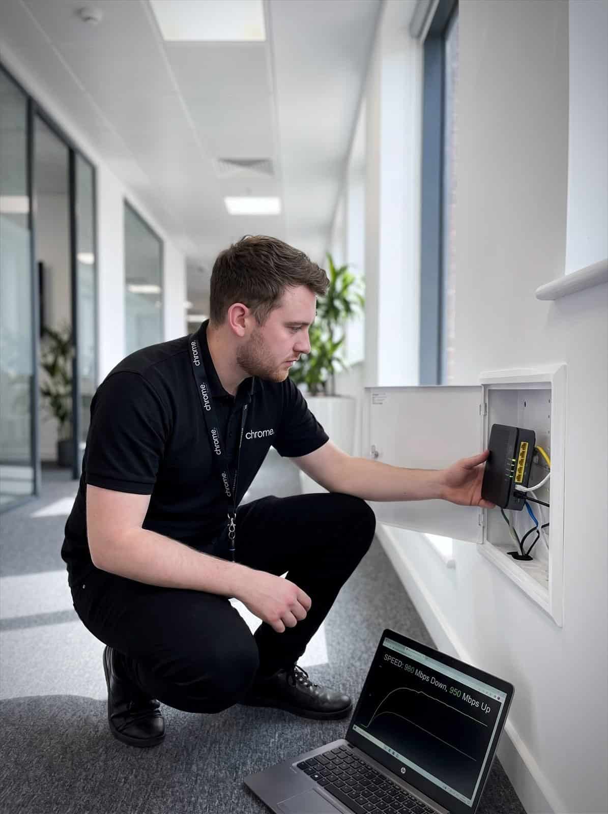 A Chrome Telecom engineer checks a business fibre router in a wall-mounted comms enclosure