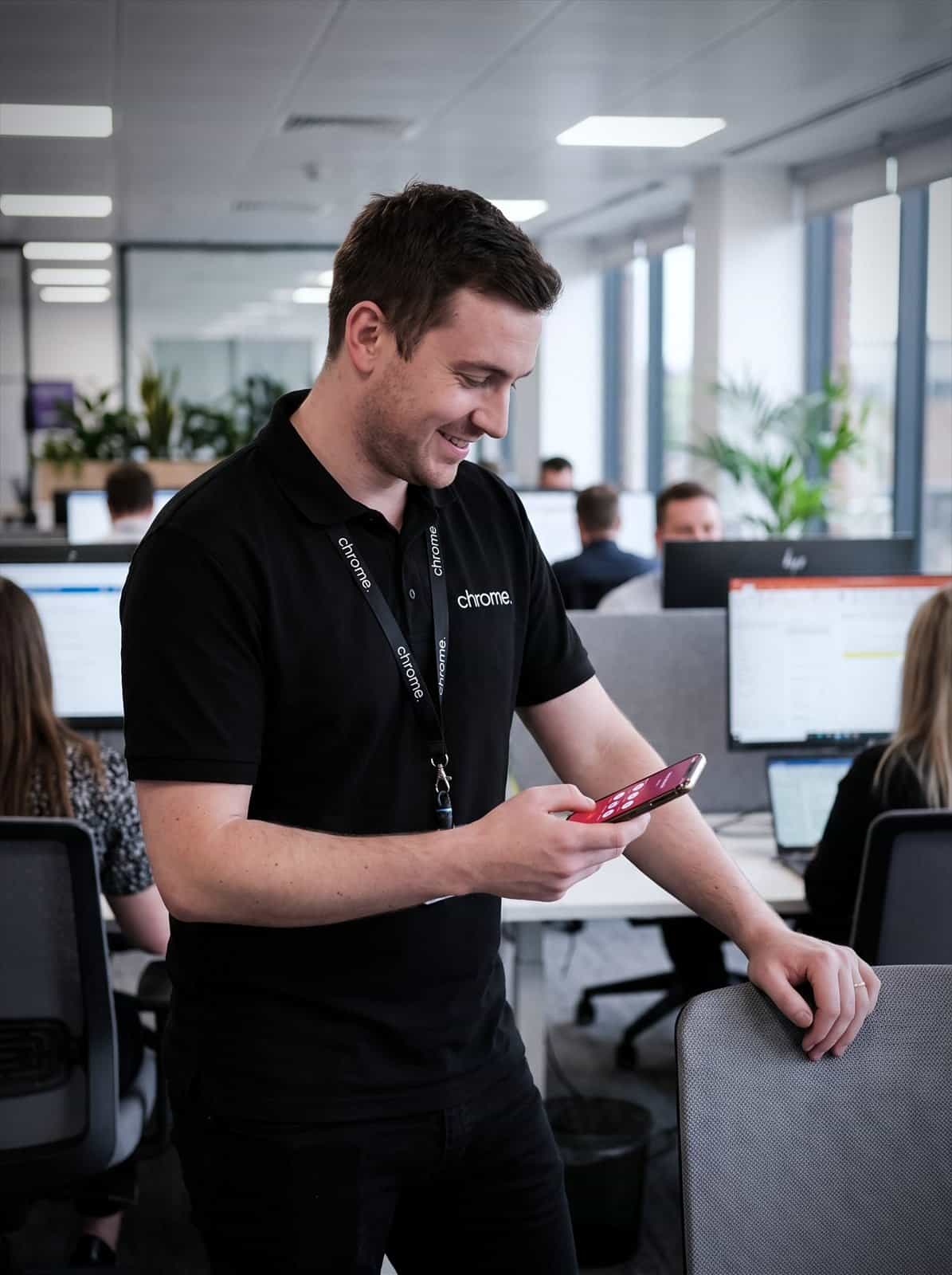 A Chrome Telecom colleague holds a smartphone running the mobile calling app in the office