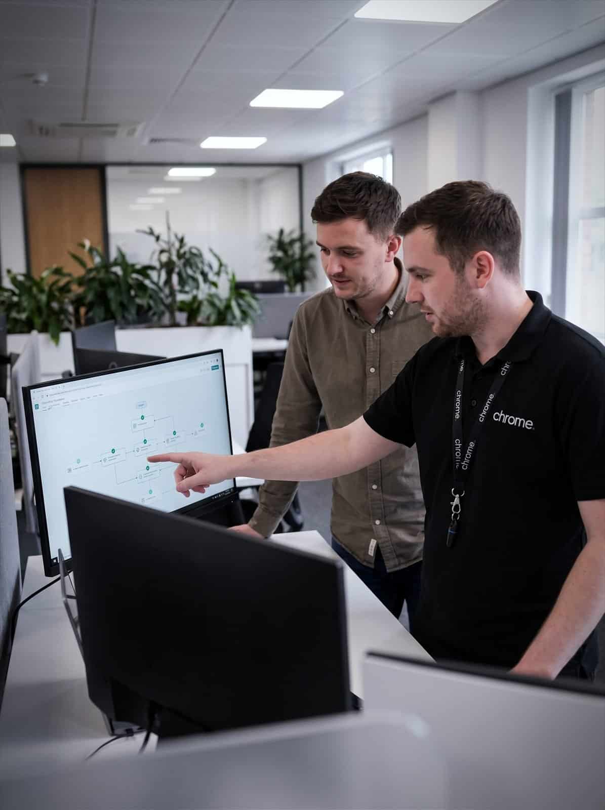 Two Chrome Telecom colleagues trace an automated workflow diagram on a monitor together