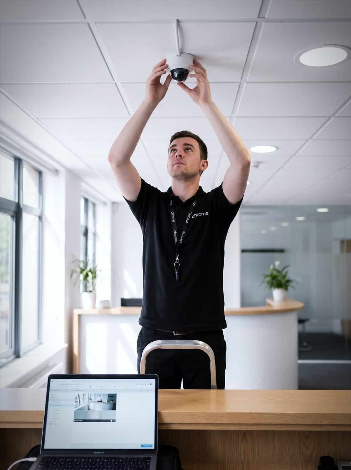 A Chrome Telecom engineer adjusts a ceiling-mounted CCTV dome camera in an office reception