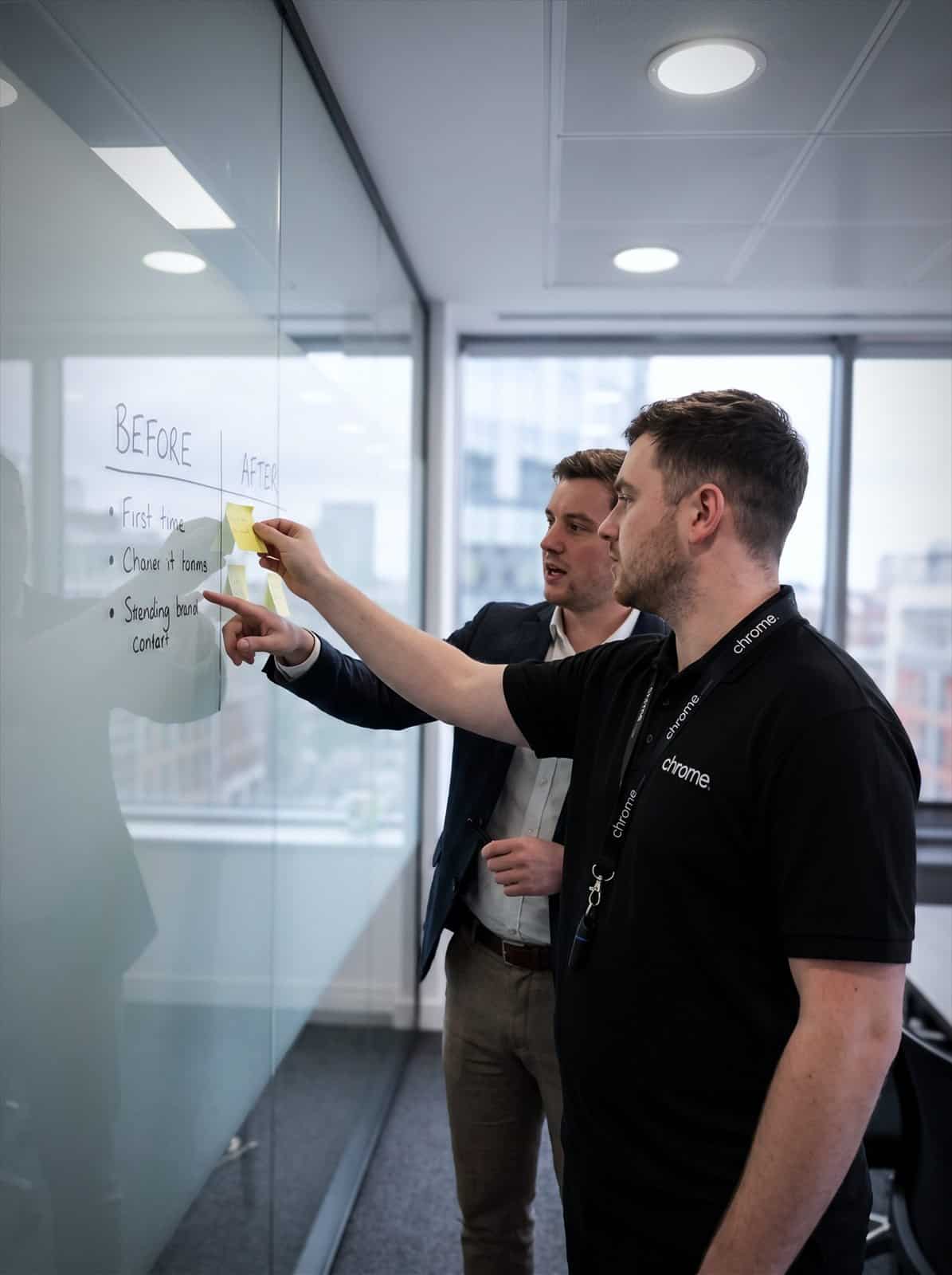 Two Chrome Telecom colleagues plan a cloud migration on a glass wall with sticky notes
