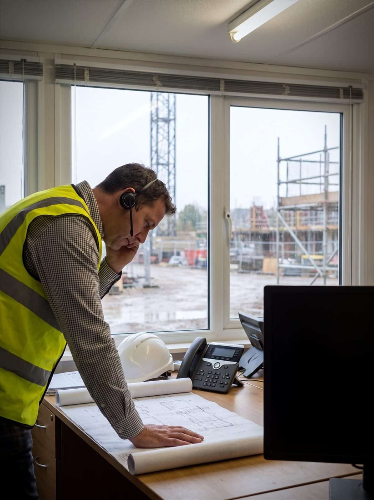 A site manager takes a call over drawings in a construction site office