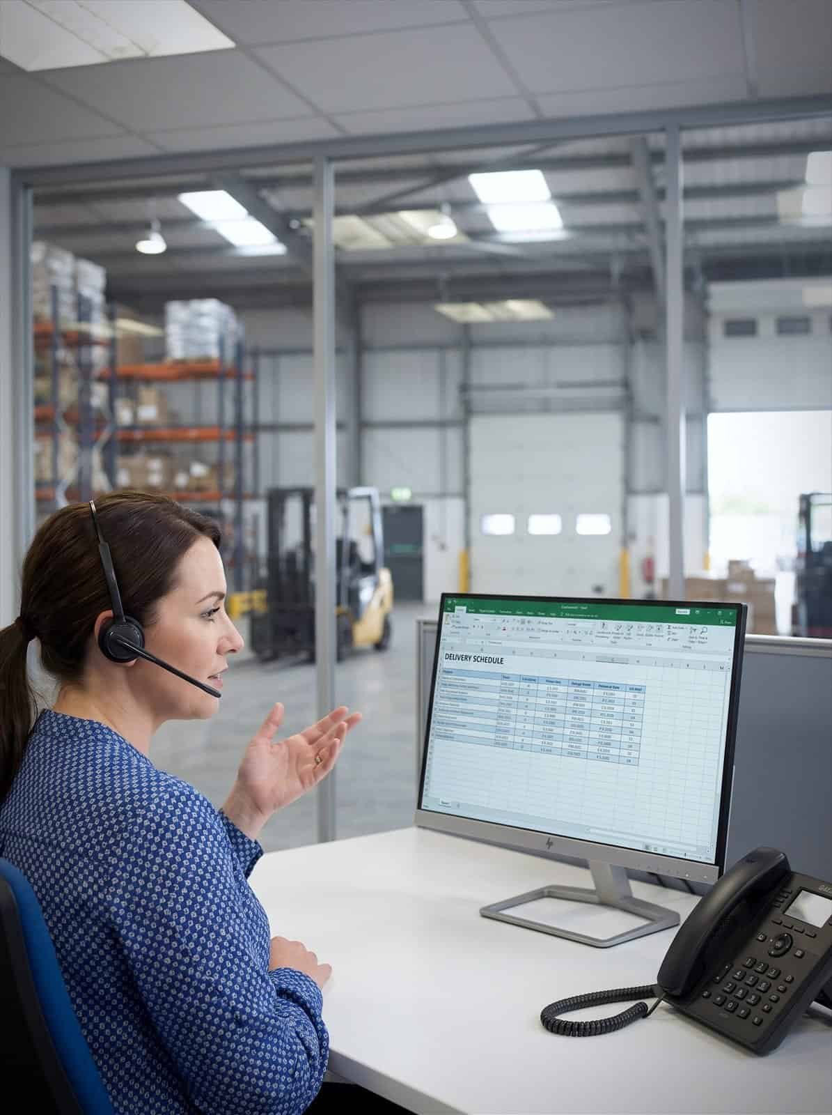 A transport coordinator takes a call in an office overlooking the warehouse