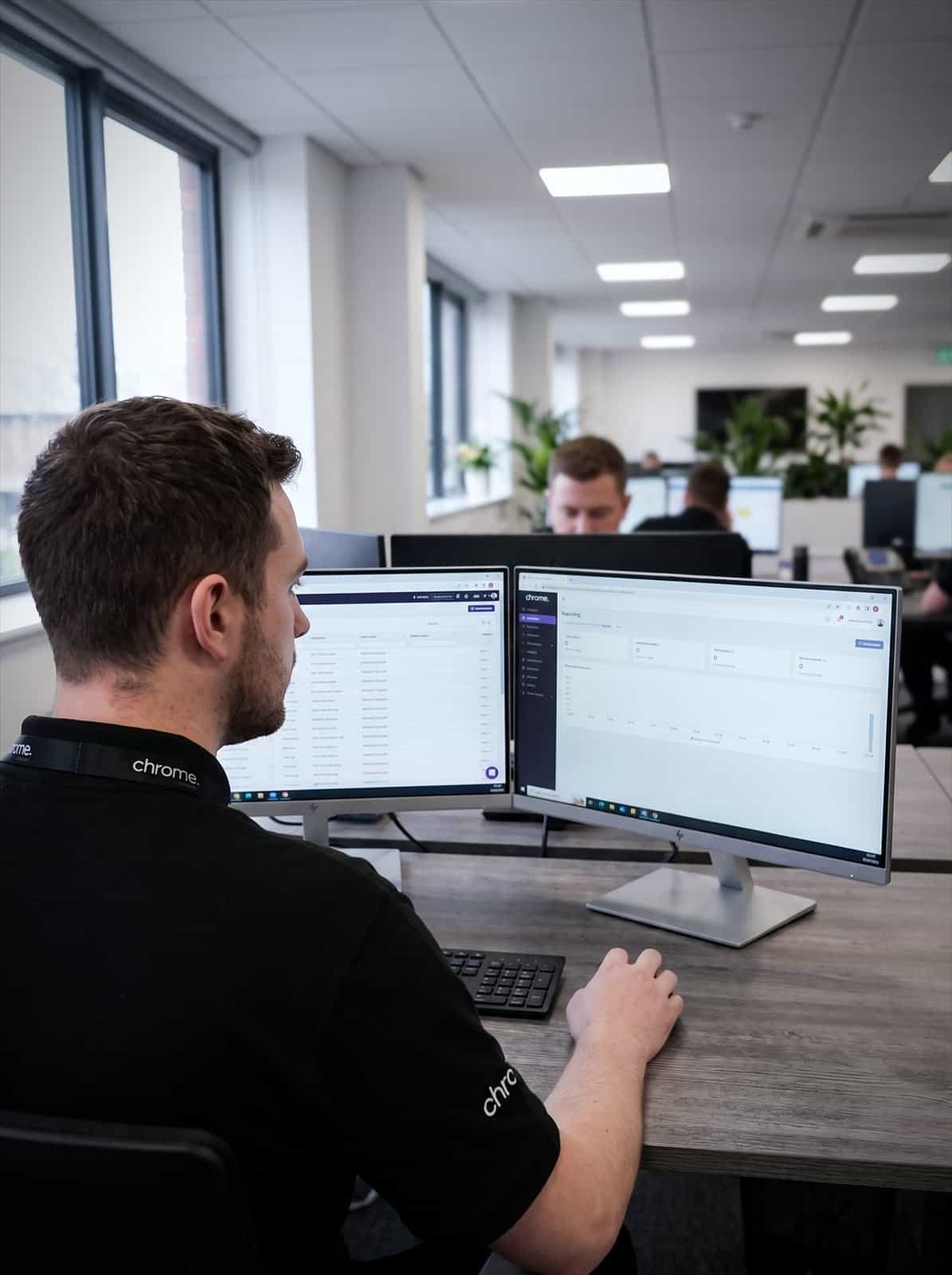 A Chrome Telecom colleague compares a customer record list and a reporting dashboard across two monitors