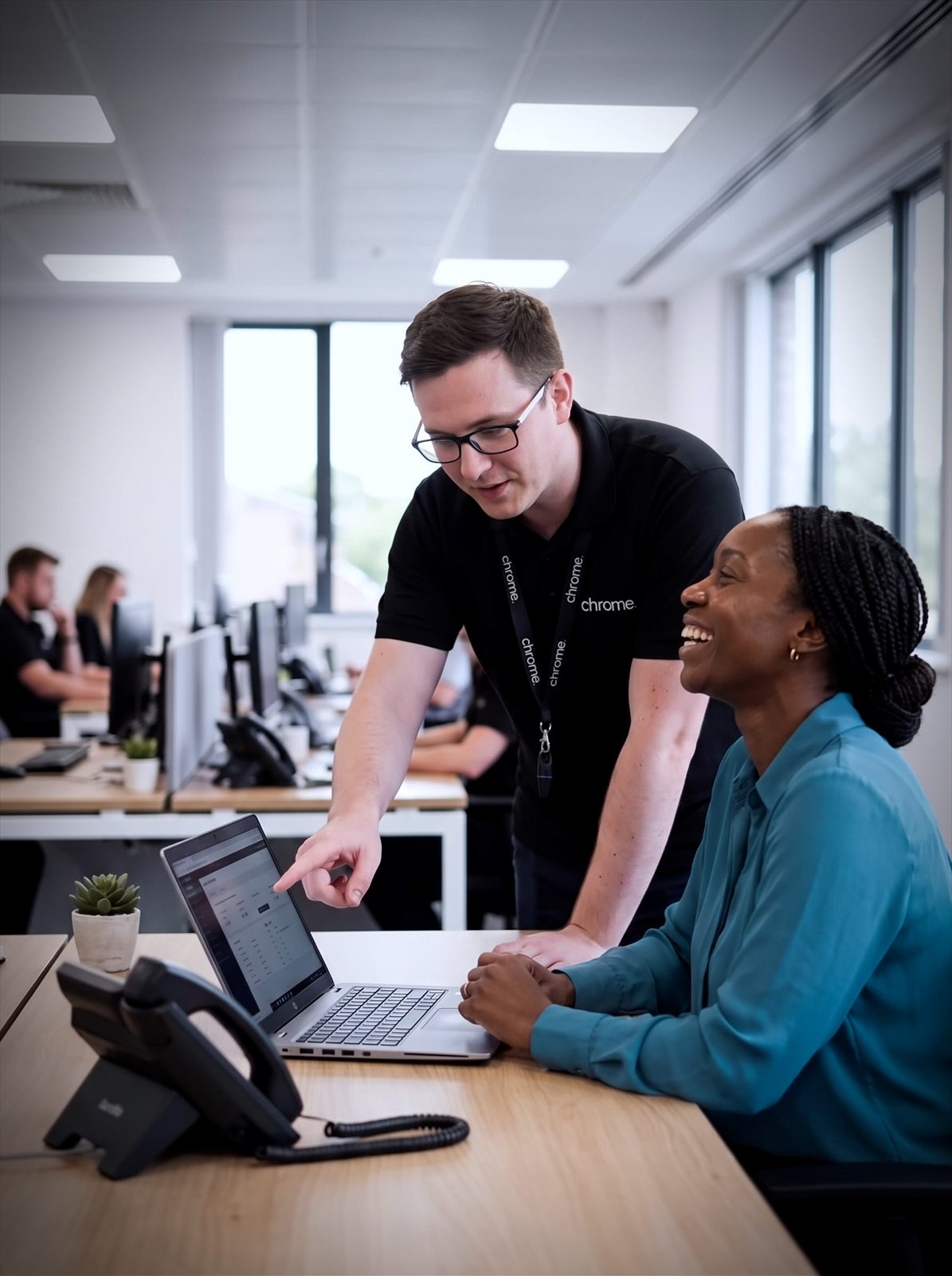 A Chrome Telecom engineer leans in to help a business customer at her laptop, both laughing