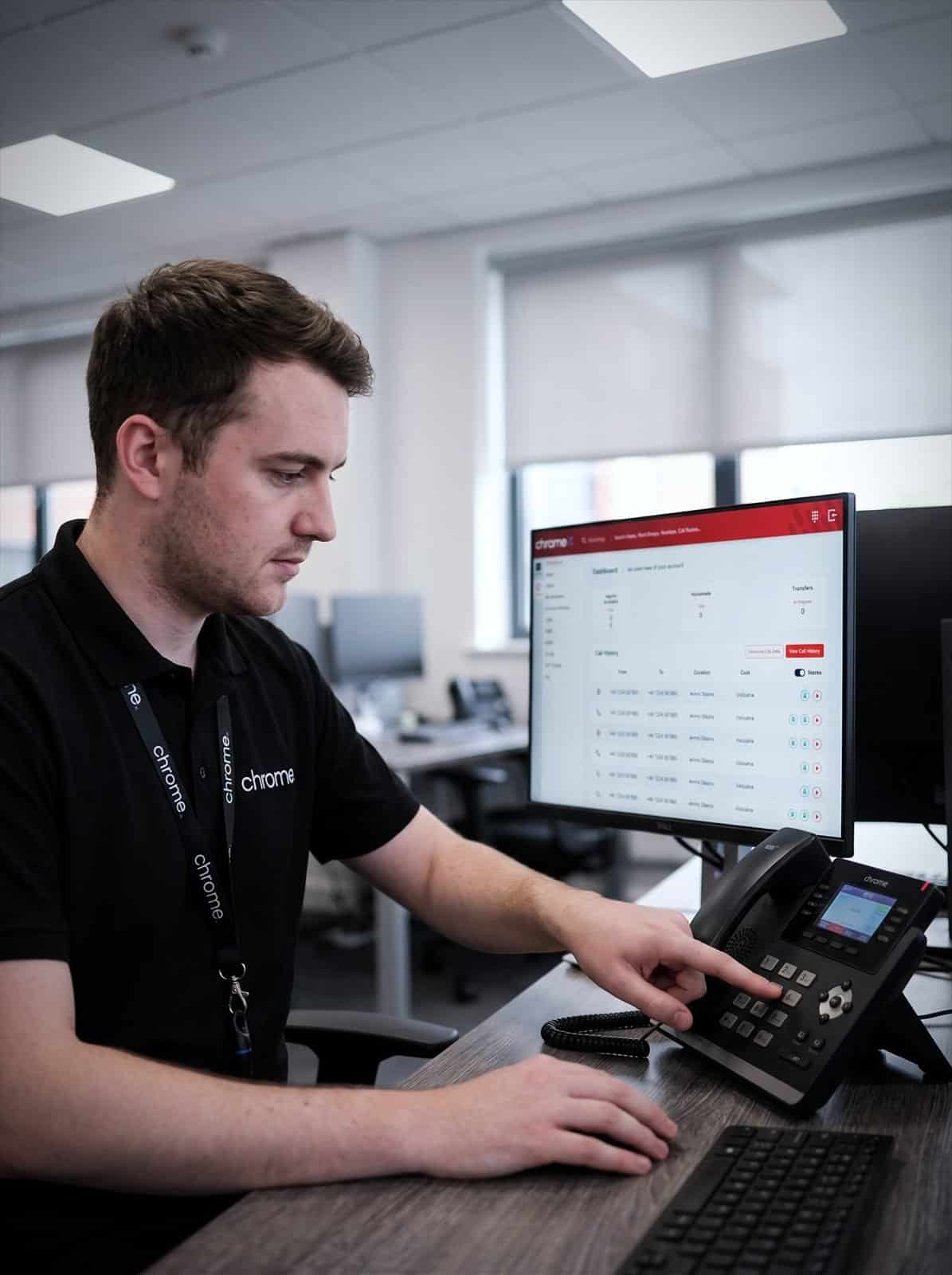 A Chrome Telecom colleague uses the keypad on a VoIP desk phone with the call dashboard open behind