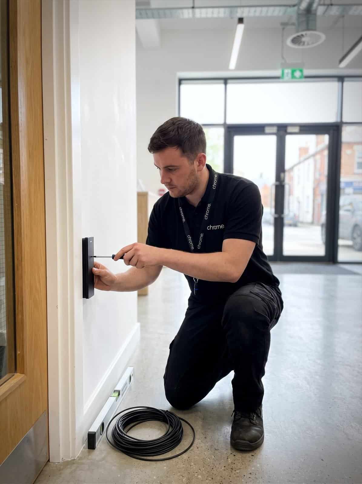 A Chrome Telecom engineer fits a door access card reader beside an office entrance