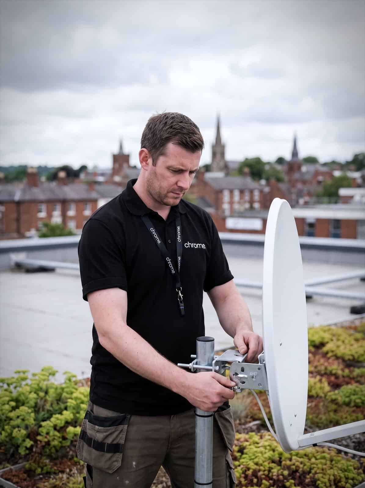 A Chrome Telecom engineer aligns a satellite internet dish on a commercial rooftop