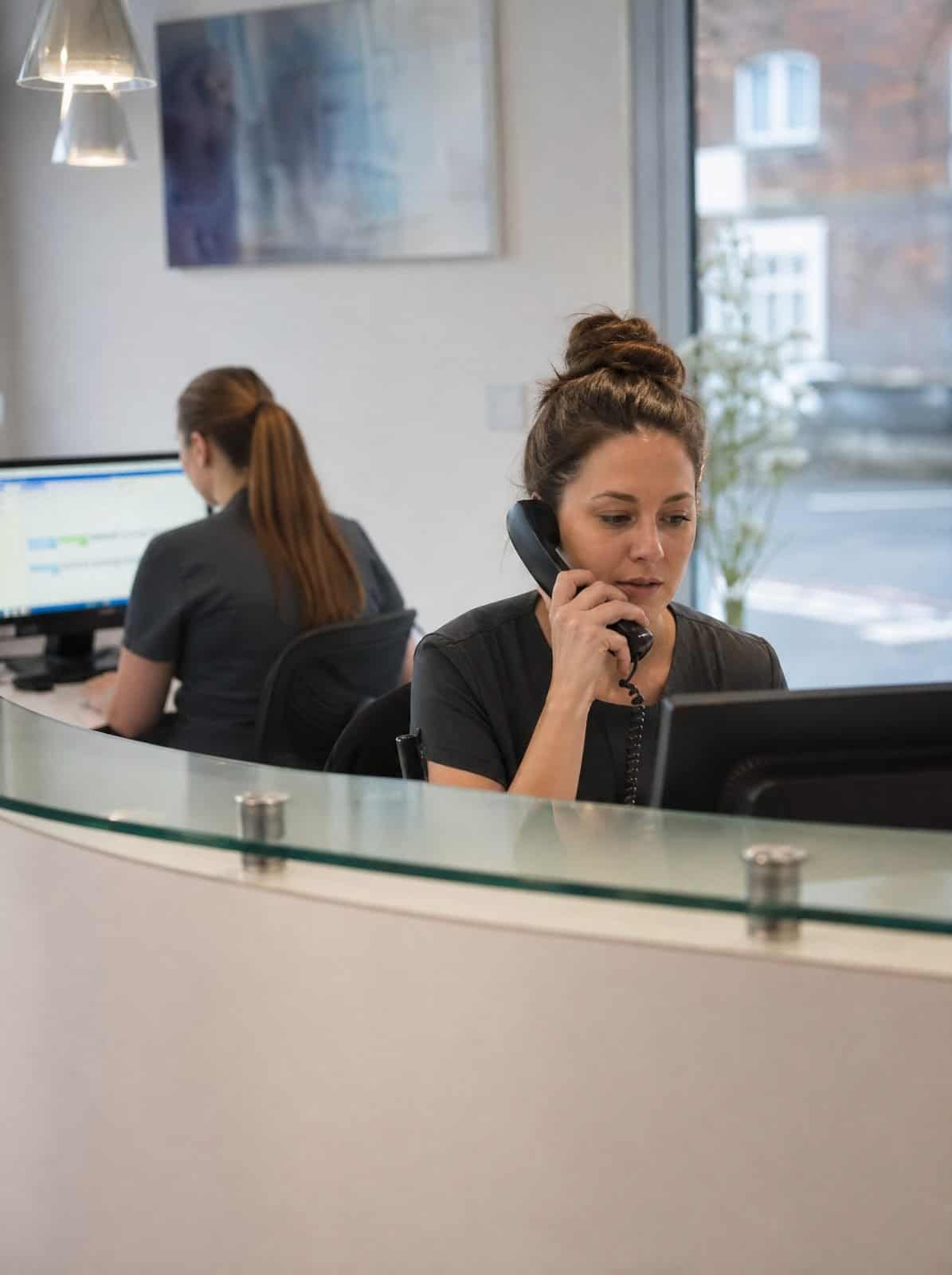 A dental practice receptionist answers a patient call at the front desk