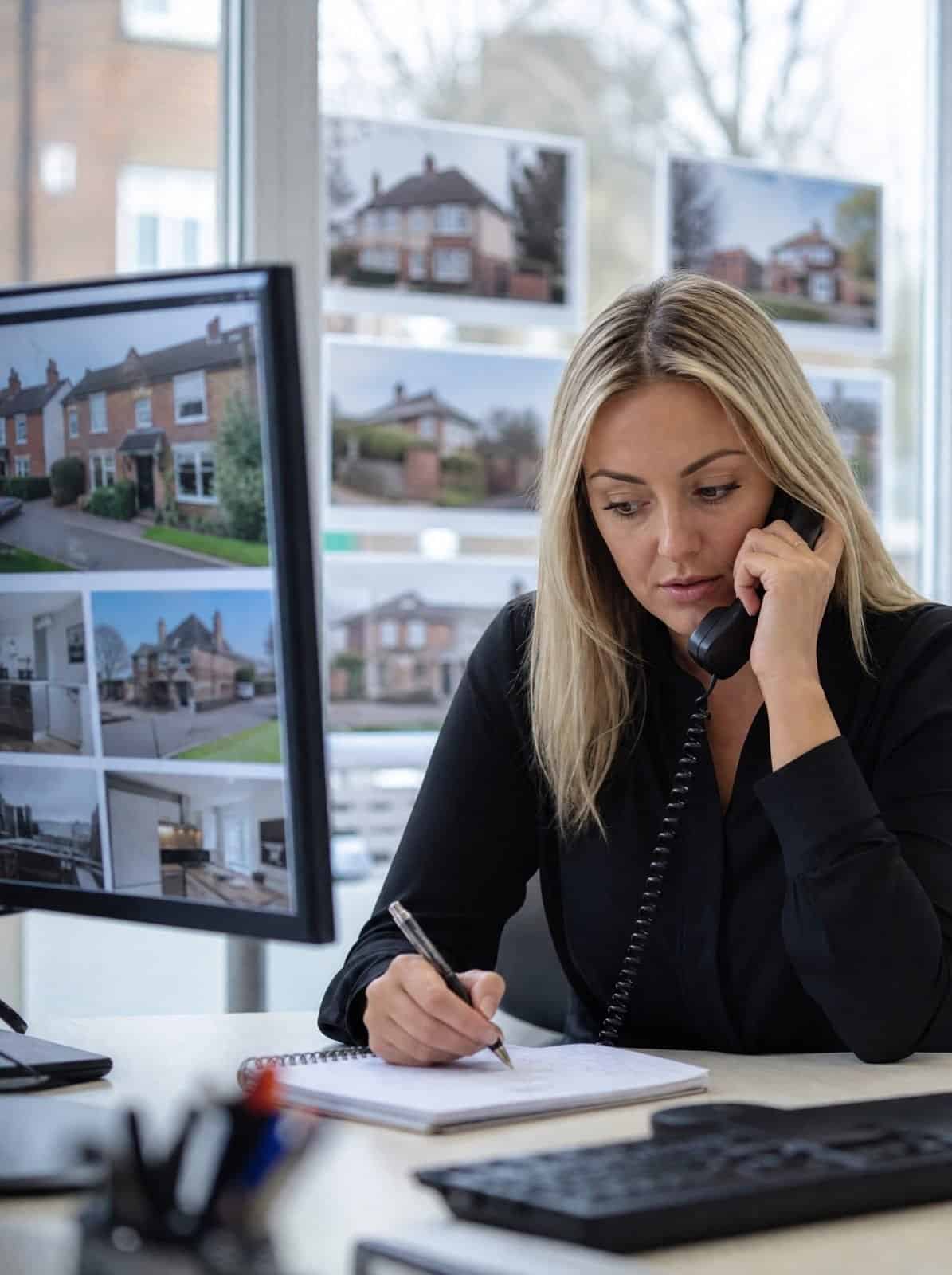 An estate agency negotiator takes a buyer enquiry at her desk