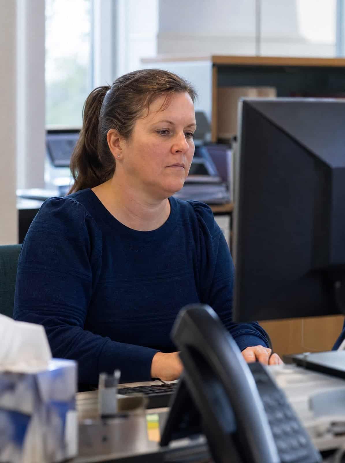 A GP practice administrator works at a computer in the back office