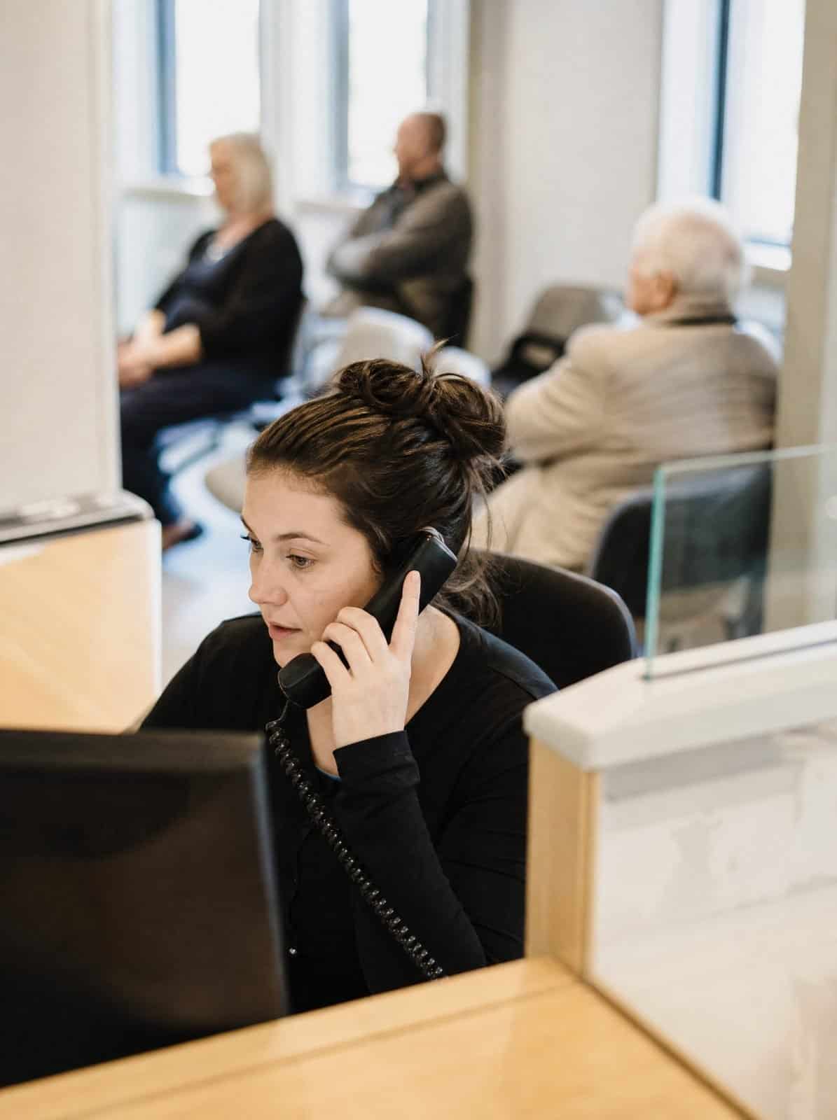 A GP surgery receptionist answers a patient call at the reception desk