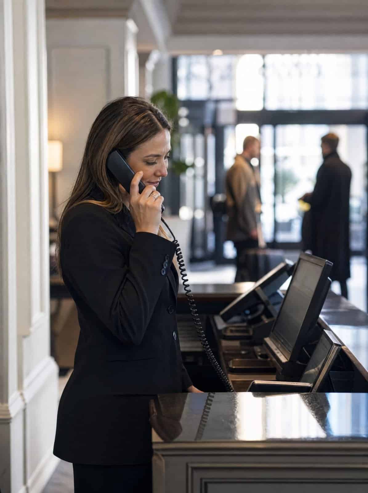 A hotel receptionist takes a booking call at the front desk