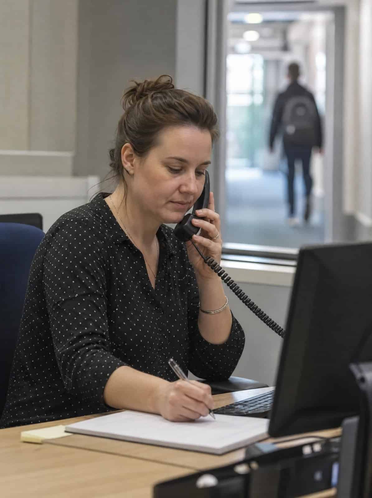 A school office administrator takes a phone call at her desk
