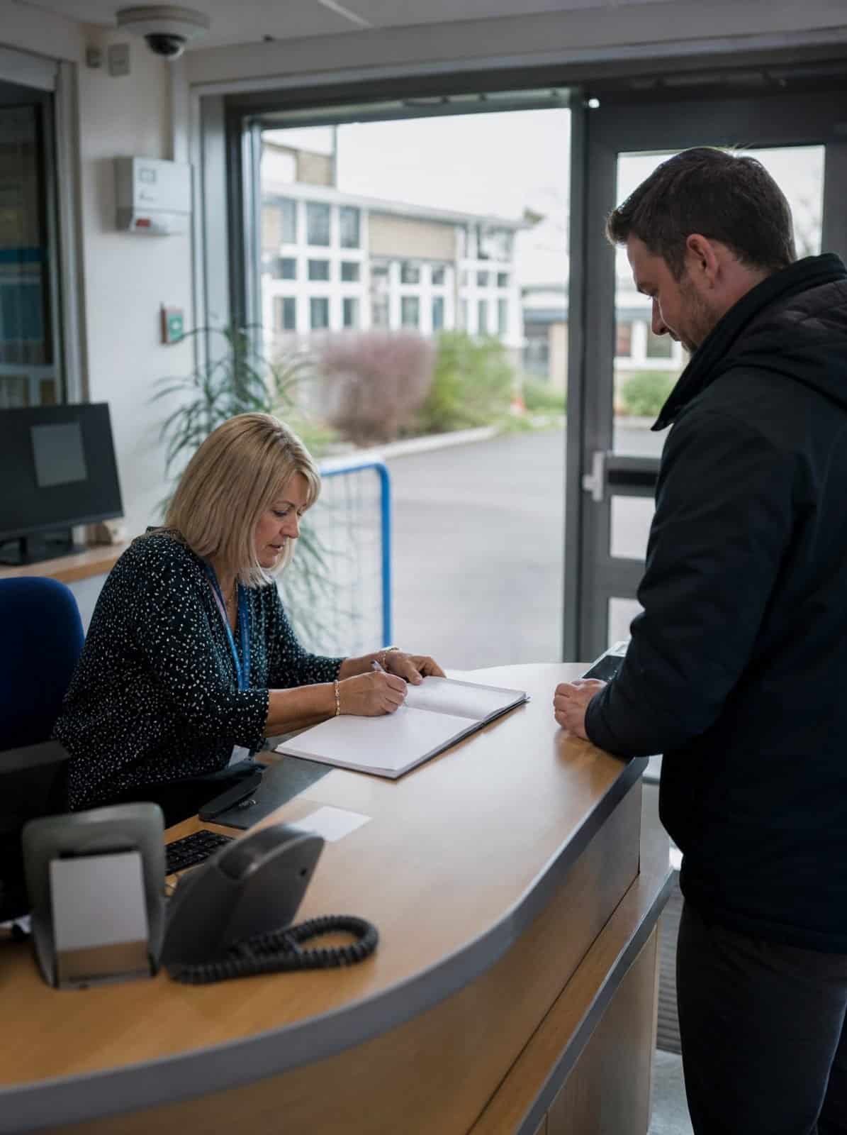 A school receptionist signs a visitor in at the front office desk