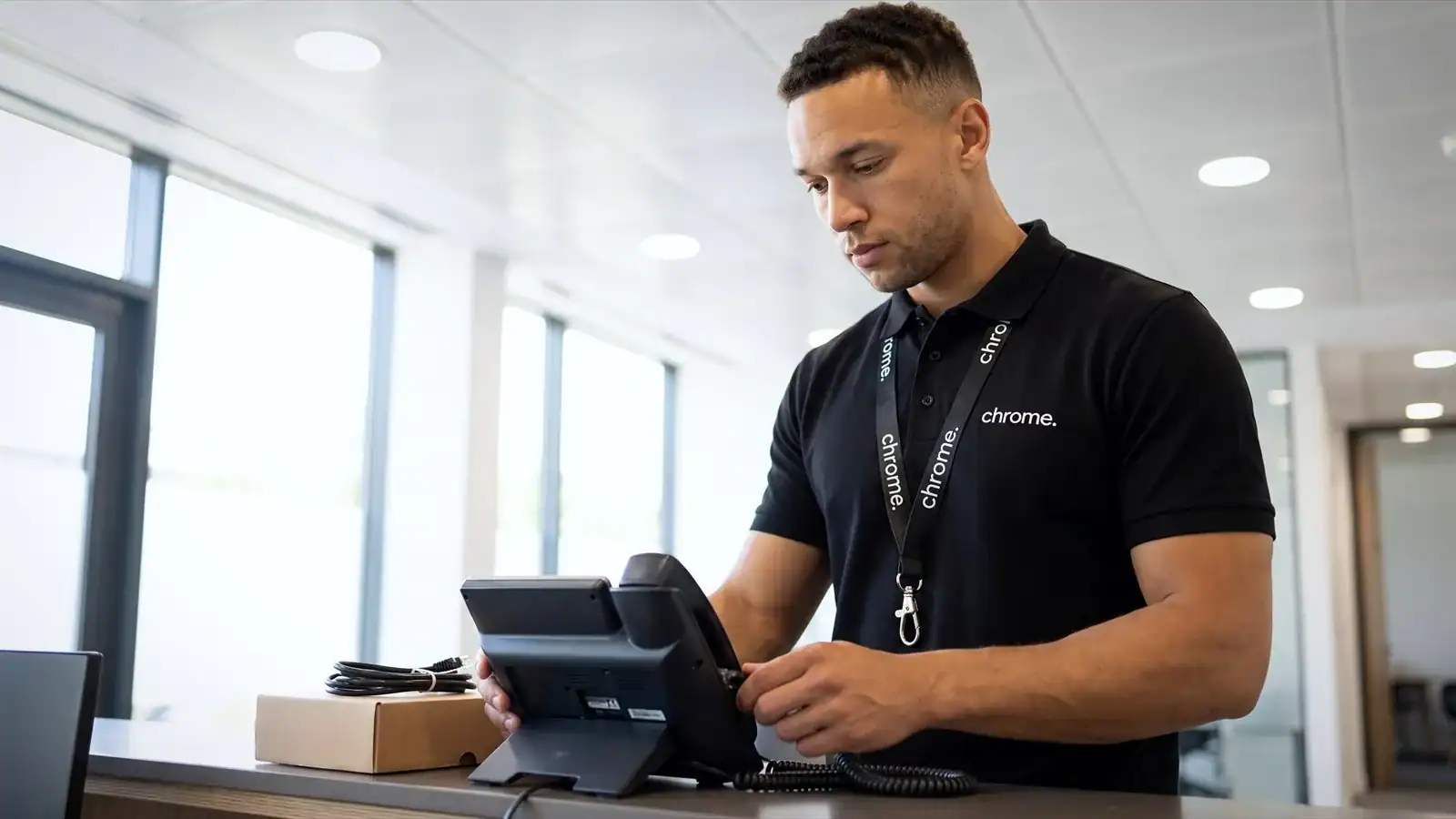 A Chrome Telecom engineer connecting a desk phone at a customer reception counter.
