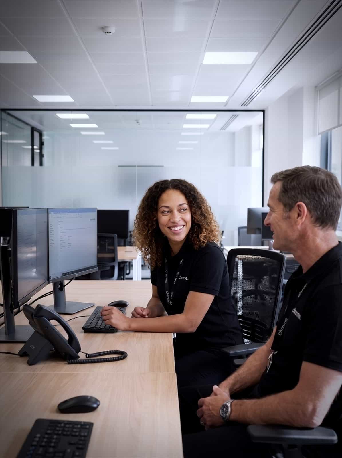 Two Chrome Telecom colleagues talking at a desk in the Whiteley office