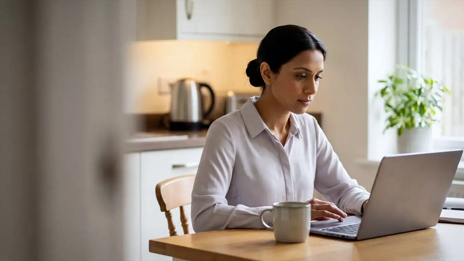 A woman working from home at a kitchen table, signing in to a work system on her laptop