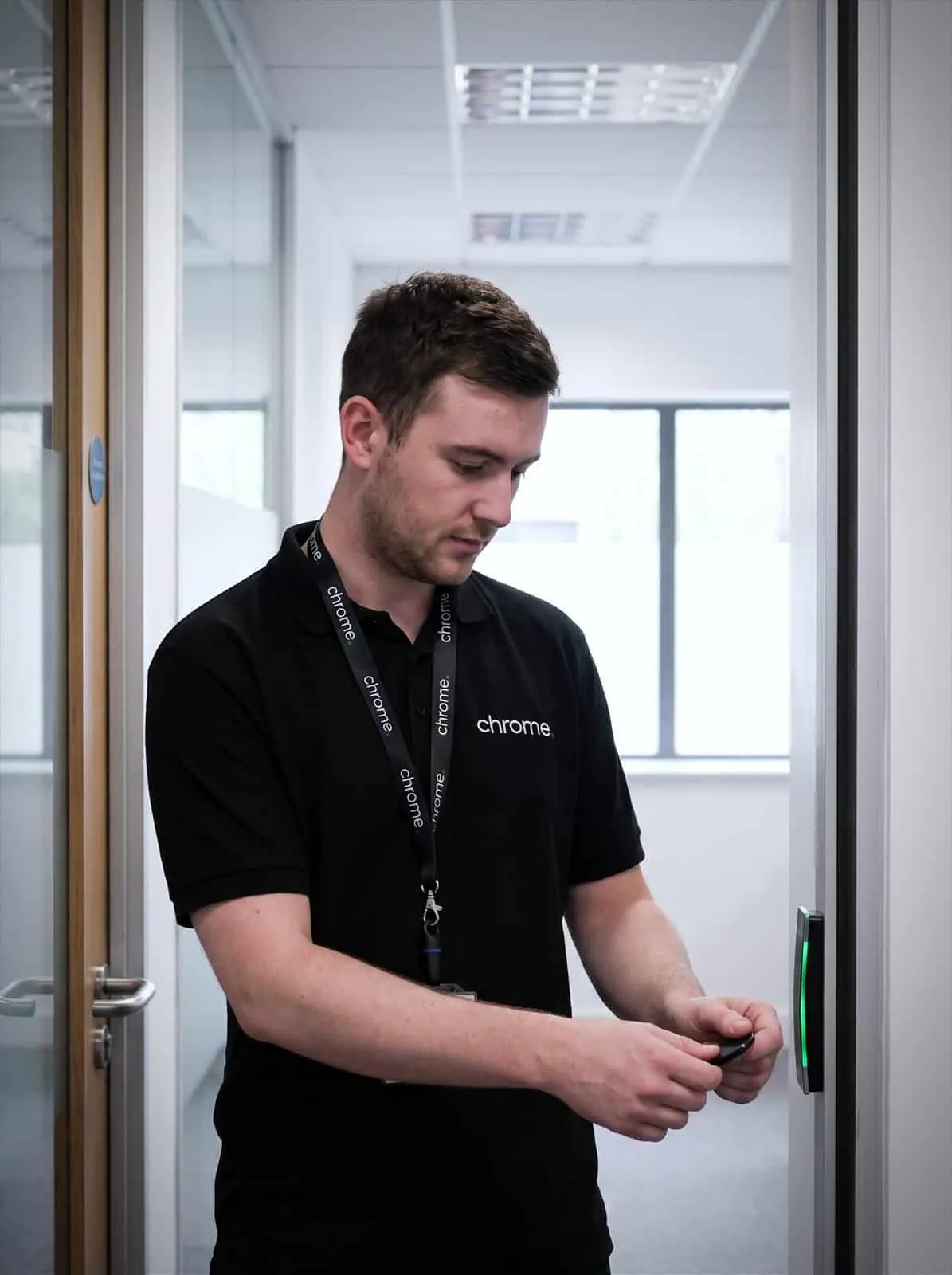 A Chrome Telecom engineer tests a door access reader with a key fob, the indicator showing green