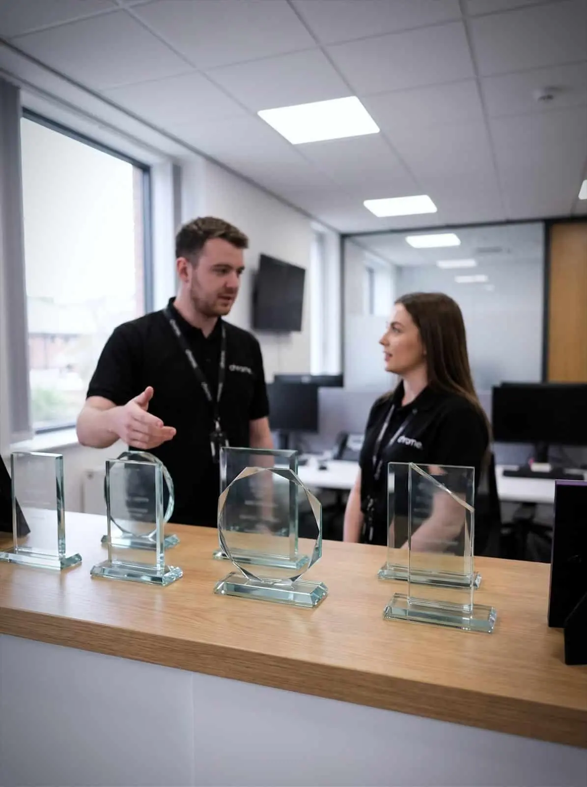 Award trophies on a shelf in the Chrome Telecom office with colleagues talking behind