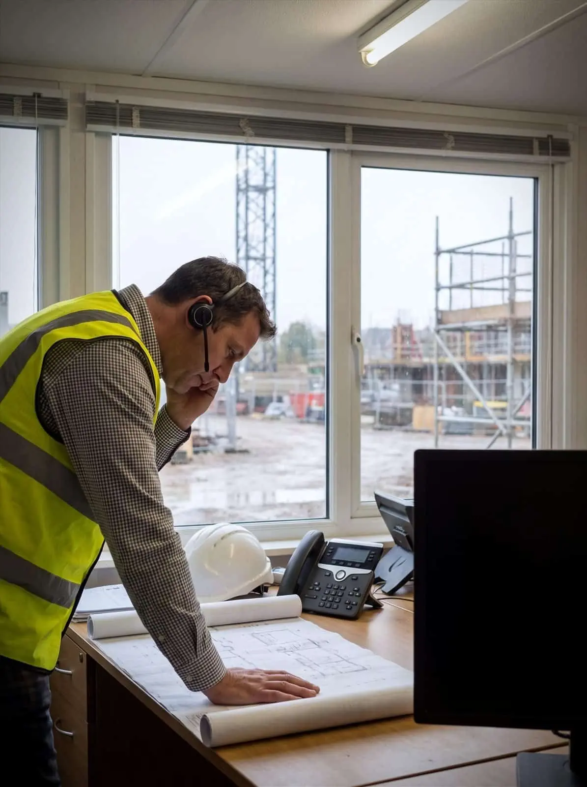 A site manager takes a call over drawings in a construction site office