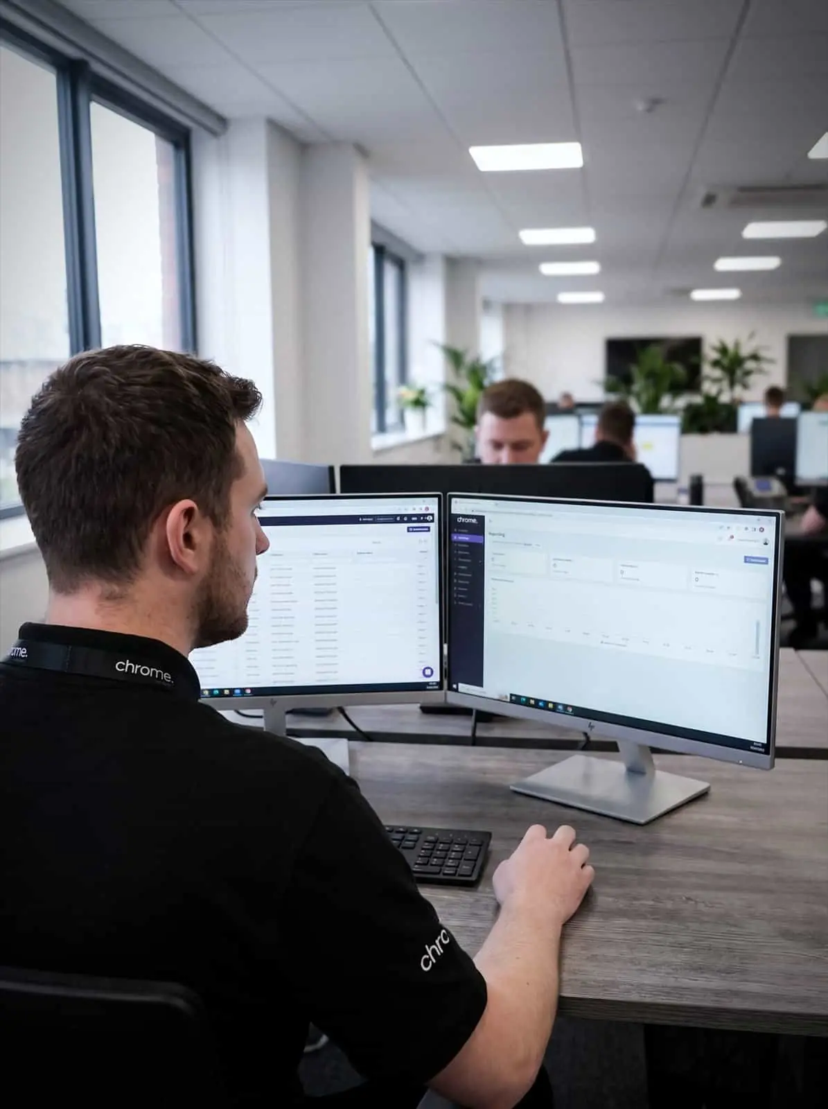 A Chrome Telecom colleague compares a customer record list and a reporting dashboard across two monitors