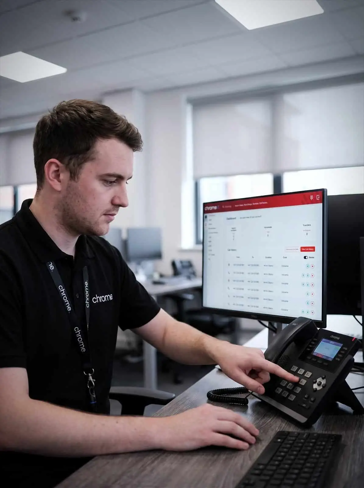 A Chrome Telecom colleague uses the keypad on a VoIP desk phone with the call dashboard open behind